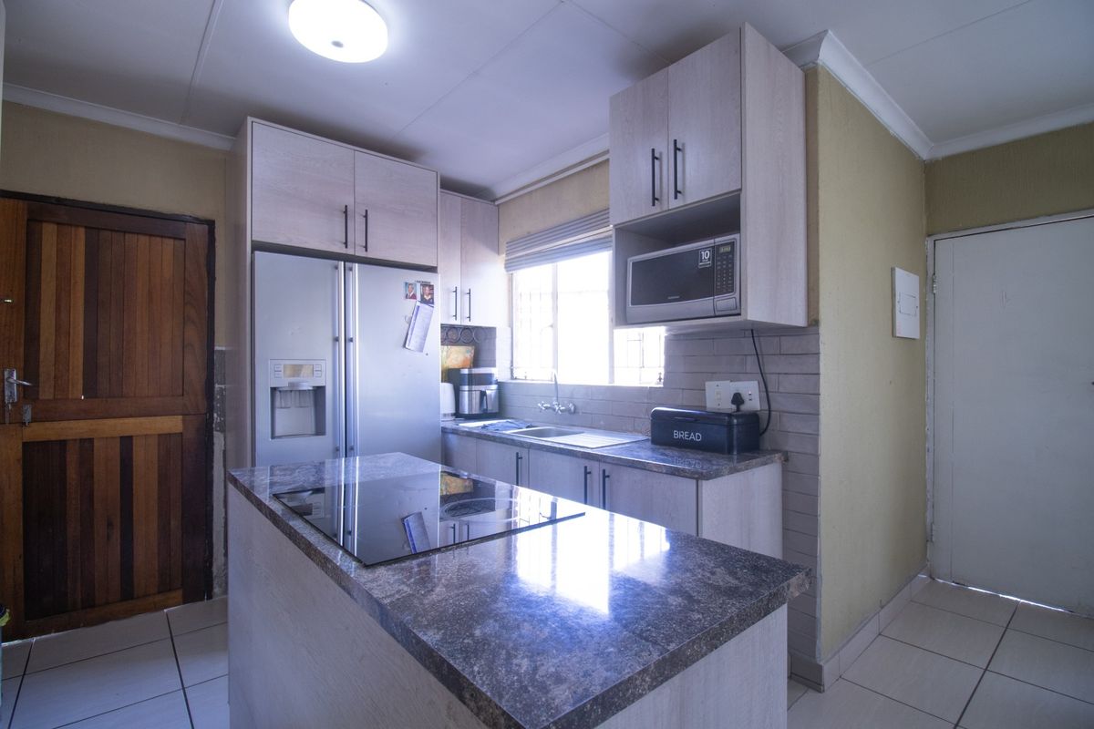 A functional kitchen featuring light-toned cabinetry, granite countertops, a central island with an integrated hob, and tiled flooring.