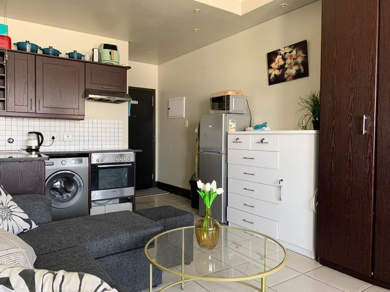 Open-plan living area featuring a compact kitchen with built-in cabinetry, tiled backsplash, and integrated appliances, seamlessly connected to the main living space.