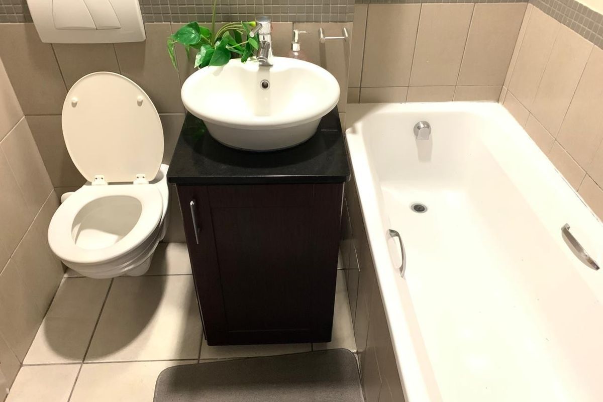 A compact bathroom featuring a wall-mounted toilet, a dark vanity cabinet with a vessel sink, and a standard bathtub with tiled finishes.