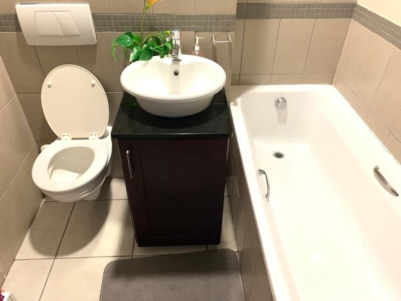 A compact bathroom featuring a wall-mounted toilet, a dark vanity cabinet with a vessel sink, and a standard bathtub with tiled finishes.