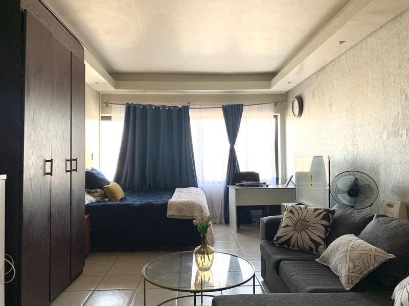 Open-plan studio apartment featuring tiled flooring, a recessed ceiling, and a large built-in wardrobe, offering a functional living and sleeping space.