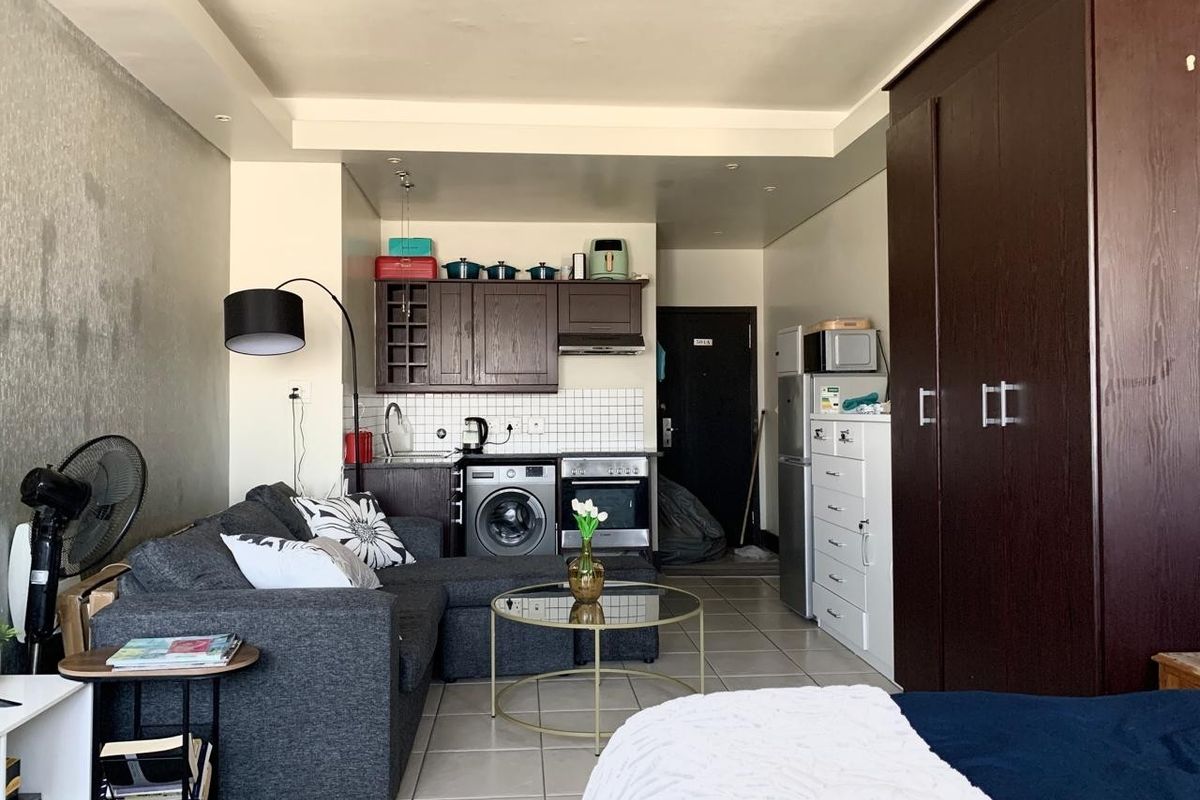 Compact open-plan studio apartment featuring a kitchenette with built-in cabinetry, oven, and hob, alongside a tiled living and sleeping area with built-in storage.