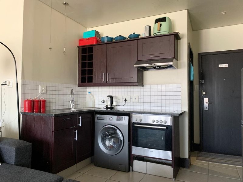 Compact kitchen featuring dark wood cabinetry, granite countertops, tiled backsplash, built-in oven, extractor fan, and an integrated washing machine.