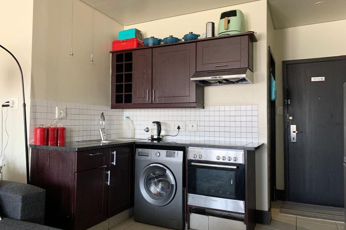 Compact kitchen featuring dark wood cabinetry, granite countertops, tiled backsplash, built-in oven, extractor fan, and an integrated washing machine.