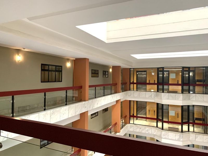 A bright, multi-level apartment building atrium featuring a central skylight, marble-clad balustrades, and glass railings overlooking the interior courtyard.