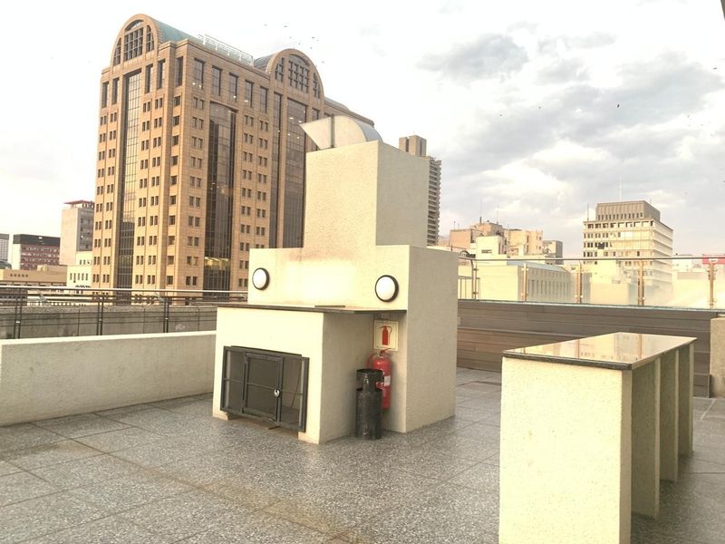 Spacious rooftop balcony featuring a built-in braai, granite prep counter, and glass balustrade with expansive city skyline views.