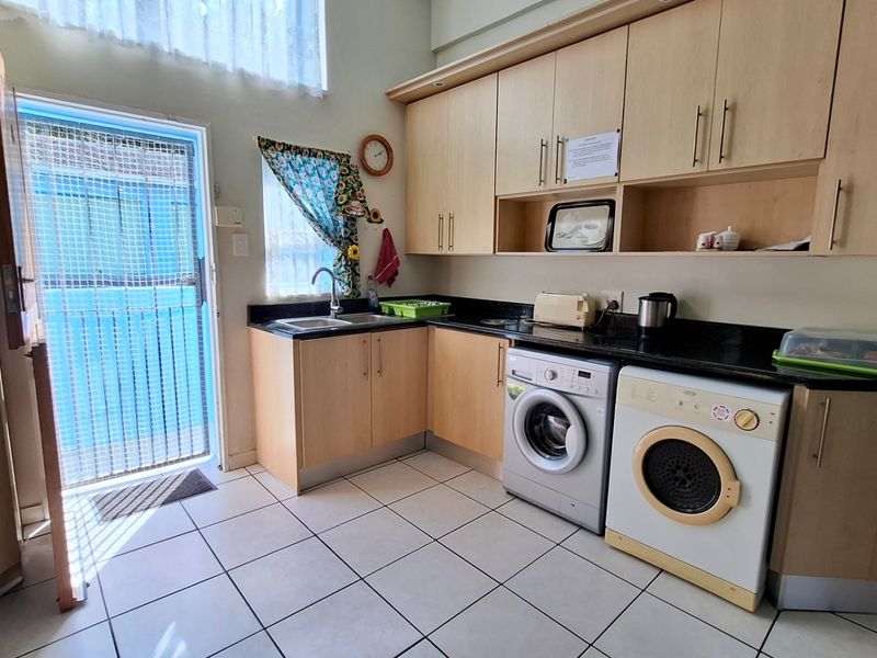 Functional laundry area featuring built-in cabinetry, granite countertops, a stainless steel sink, and tiled flooring with direct access to an exterior security gate.