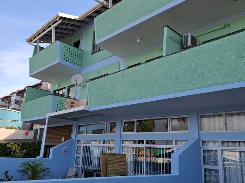 Exterior view of an apartment building featuring multiple balconies, sliding glass doors with security gates, and an external air conditioning unit.
