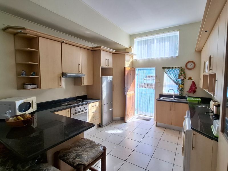 A functional kitchen featuring light wood cabinetry, dark granite countertops, built-in oven and hob, and tiled flooring with direct access to the exterior.