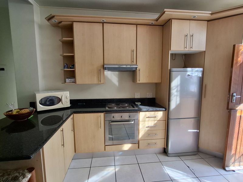Functional kitchen featuring light wood cabinetry, granite countertops, built-in oven, electric hob, and tiled flooring with direct access to an exterior door.
