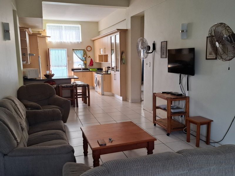 Open-plan living and kitchen area featuring tiled flooring, built-in cabinetry, and a breakfast counter, offering a functional and connected living space.