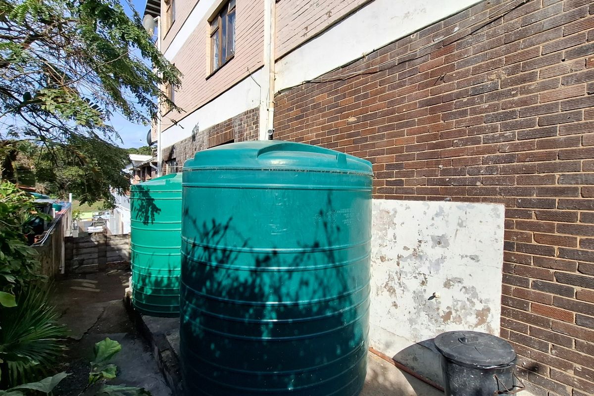 Rear exterior area featuring two large green water storage tanks positioned against a brick building facade with some visible wall surface wear.