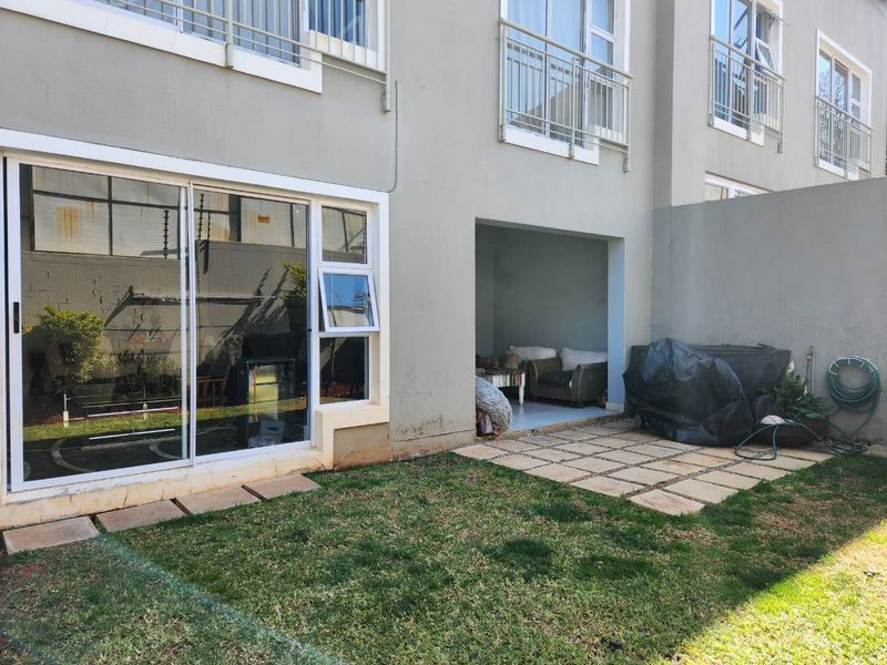 Rear view of the apartment featuring a small private garden, paved patio area, and sliding door access to the interior living space.