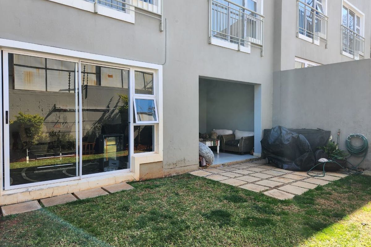 Rear view of the apartment featuring a small private garden, paved patio area, and sliding door access to the interior living space.