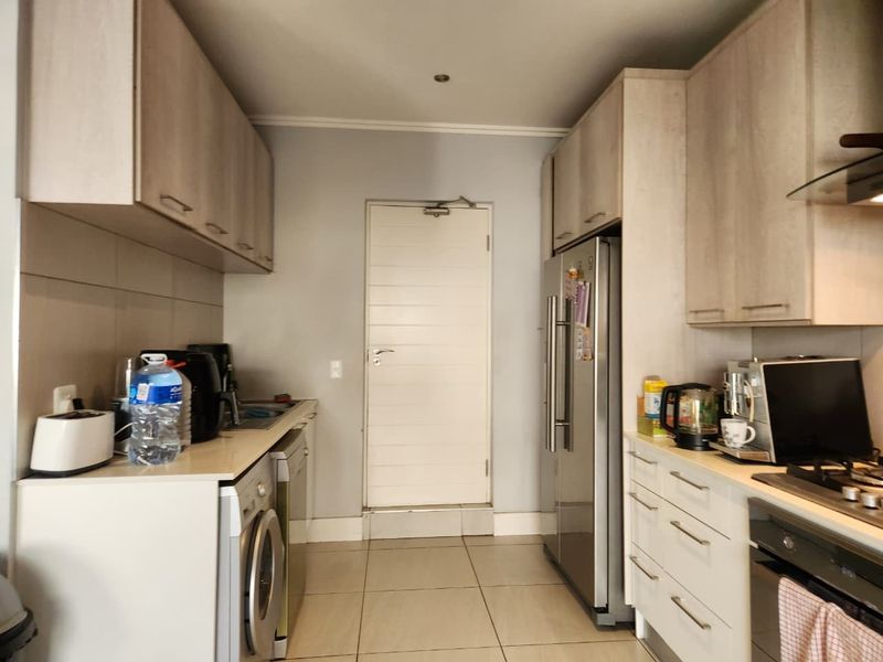 A functional galley-style kitchen featuring light wood-finish cabinetry, tiled flooring, built-in oven, gas hob, and dedicated space for a large refrigerator.