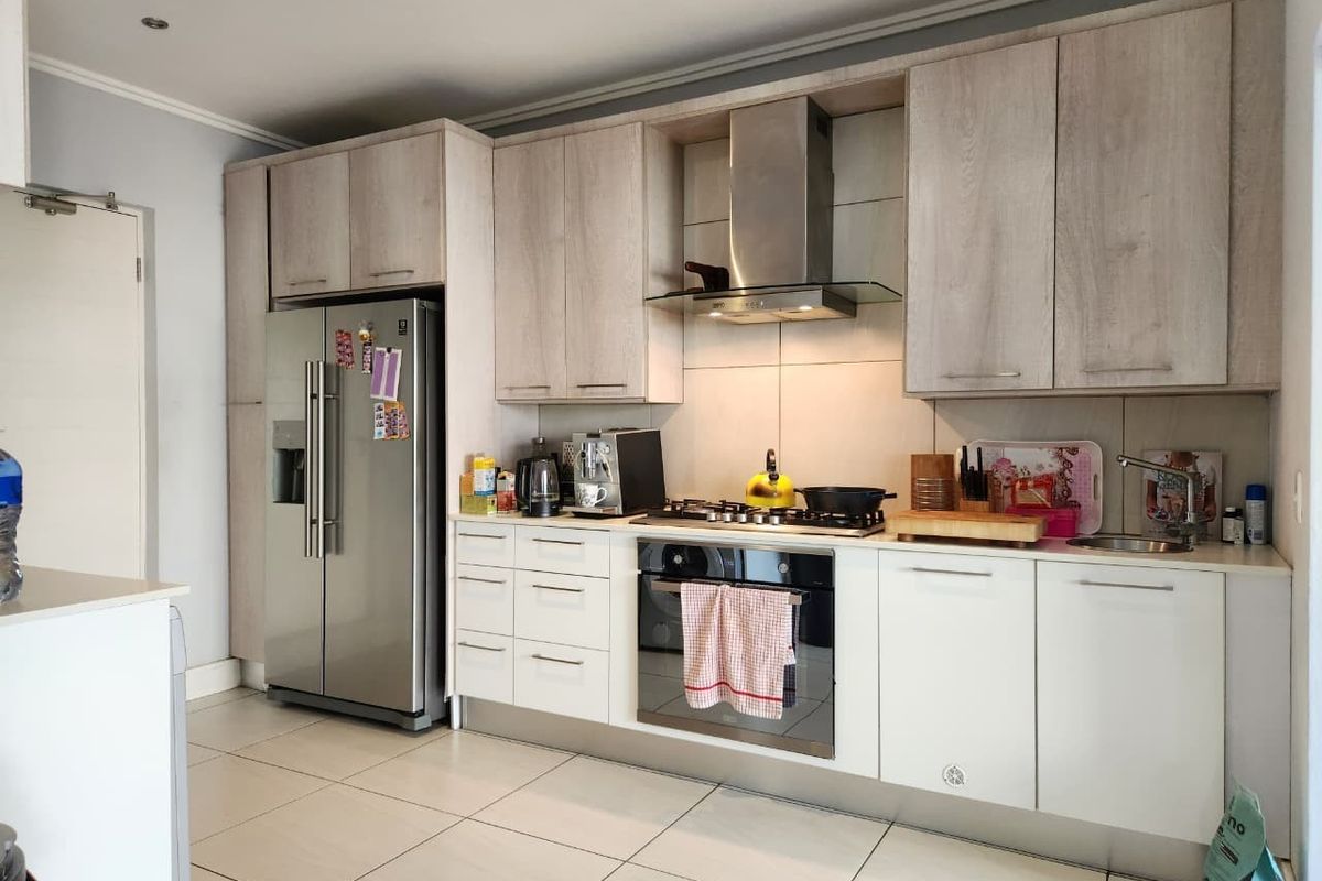 Modern kitchen featuring light wood-grain cabinetry, stainless steel appliances including a gas hob and extractor fan, and neutral tiled flooring.