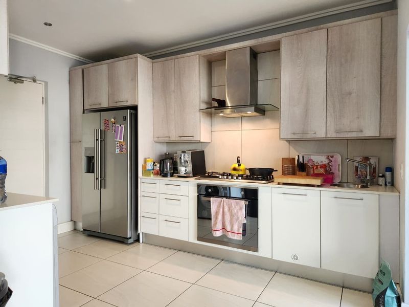 Modern kitchen featuring light wood-grain cabinetry, stainless steel appliances including a gas hob and extractor fan, and neutral tiled flooring.