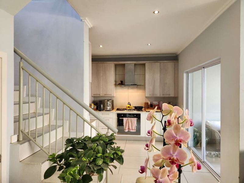 Open plan kitchen featuring light wood cabinetry, built-in oven, and hob, adjacent to a staircase and sliding doors leading to an outdoor area.