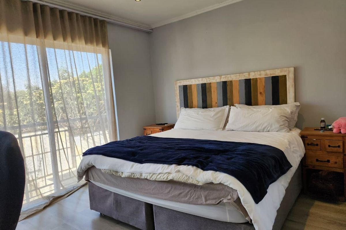 A well-lit bedroom featuring laminate flooring, recessed downlights, and a large sliding glass door providing access to an outdoor area.