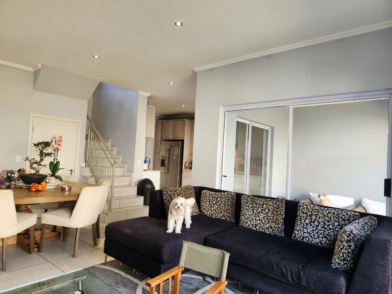 An open-plan living and dining area featuring tiled floors, recessed lighting, a staircase, and sliding glass doors leading to an outdoor space.