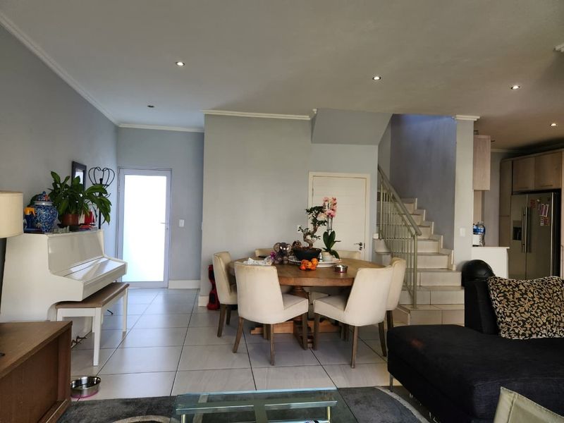 Open-plan living and dining area featuring tiled floors, recessed lighting, and a staircase leading to the upper level, adjacent to a modern kitchen.