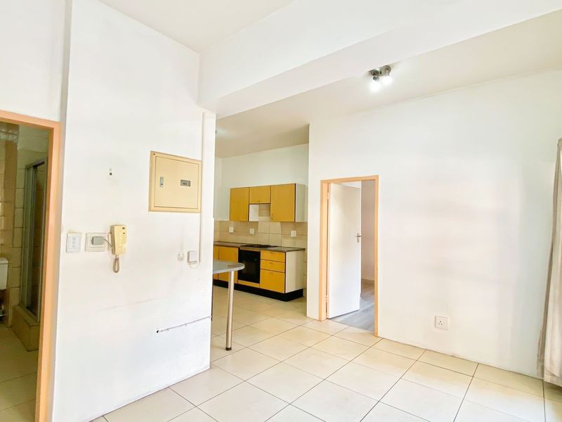 Open-plan living area featuring tiled flooring and a functional kitchen with built-in cabinetry, oven, and hob, adjacent to a bathroom entrance.
