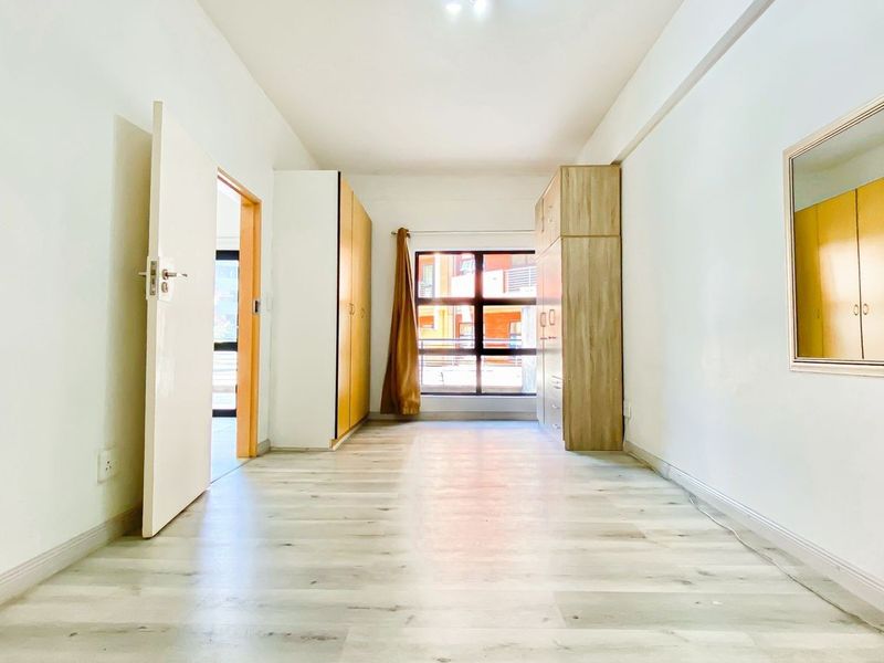 A bright, empty bedroom featuring light-toned laminate flooring and built-in wooden cupboards, offering a clean and neutral space ready for personalization.