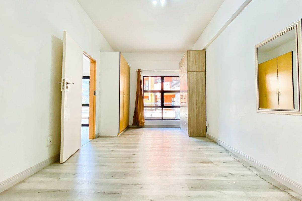 A bright, empty bedroom featuring light-toned laminate flooring and built-in wooden cupboards, offering a clean and neutral space ready for personalization.