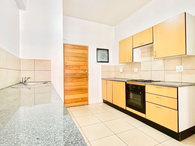 A functional kitchen featuring light wood cabinetry, granite countertops, built-in oven and hob, and neutral tiled flooring and backsplash.