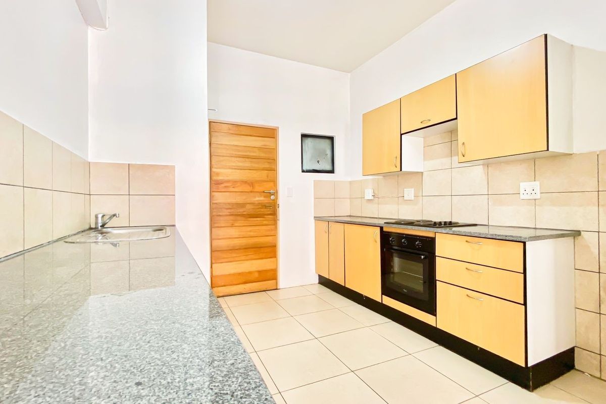 A functional kitchen featuring light wood cabinetry, granite countertops, built-in oven and hob, and neutral tiled flooring and backsplash.