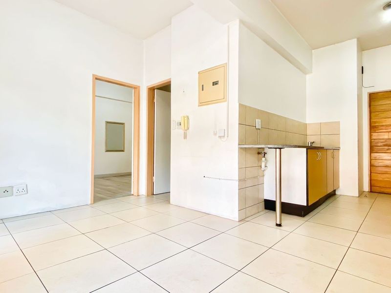 An open-plan living and kitchen area featuring tiled flooring, basic cabinetry, and neutral walls, offering a blank canvas for potential renovation.