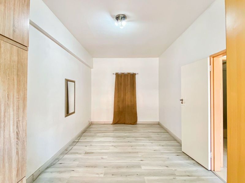 A bright, empty bedroom featuring light-toned laminate flooring and a built-in wooden wardrobe, offering a clean and neutral space ready for personalization.
