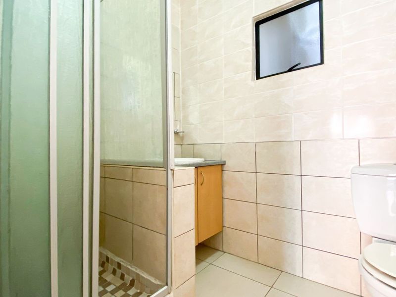 A functional bathroom featuring a shower enclosure, vanity cabinet, and toilet with neutral wall and floor tiling.