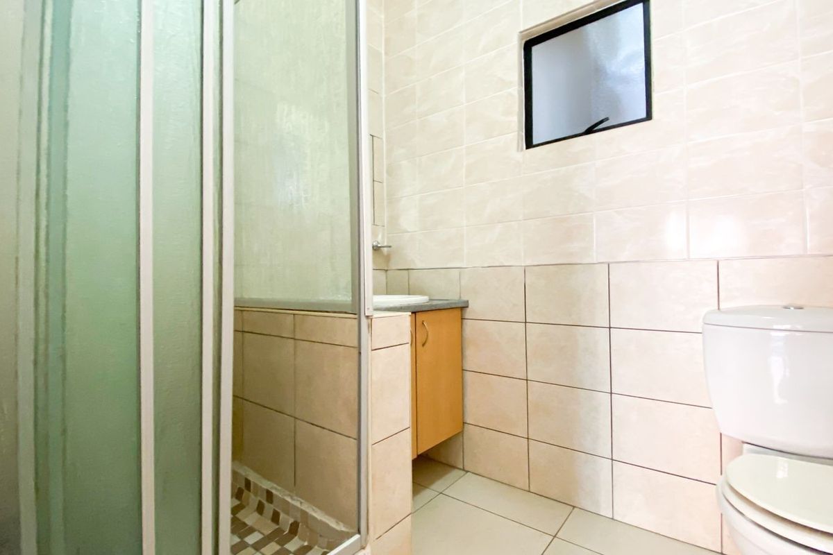 A functional bathroom featuring a shower enclosure, vanity cabinet, and toilet with neutral wall and floor tiling.