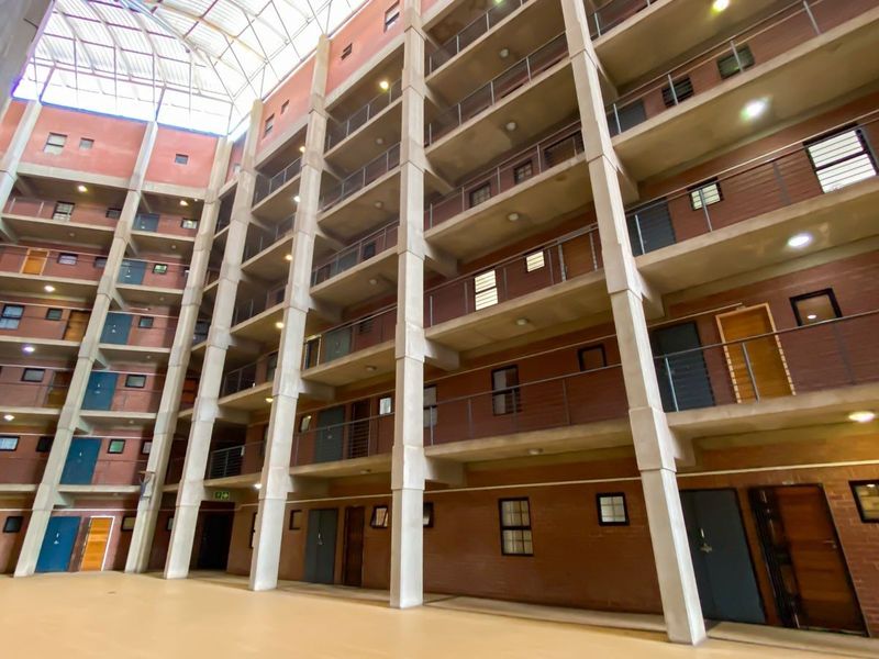 A view of the apartment complex atrium featuring a large skylight, multi-level walkways, and exposed brick architecture.