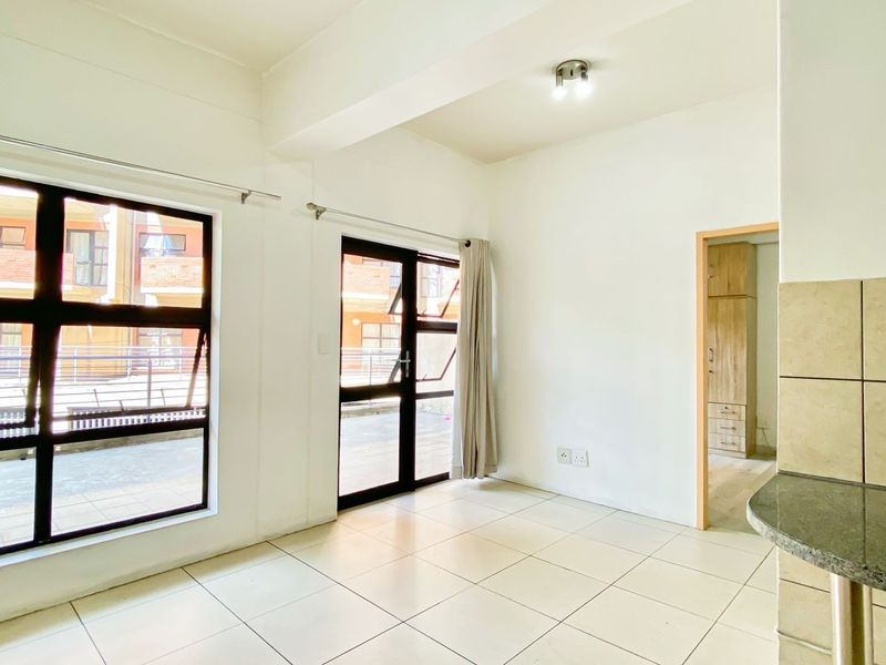 Bright open-plan living area featuring tiled floors, a granite breakfast counter, and large aluminium windows and doors leading to an outdoor space.