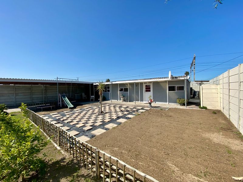 Rear exterior view of the property featuring a paved patio area, corrugated roof structure, and a fenced garden space.