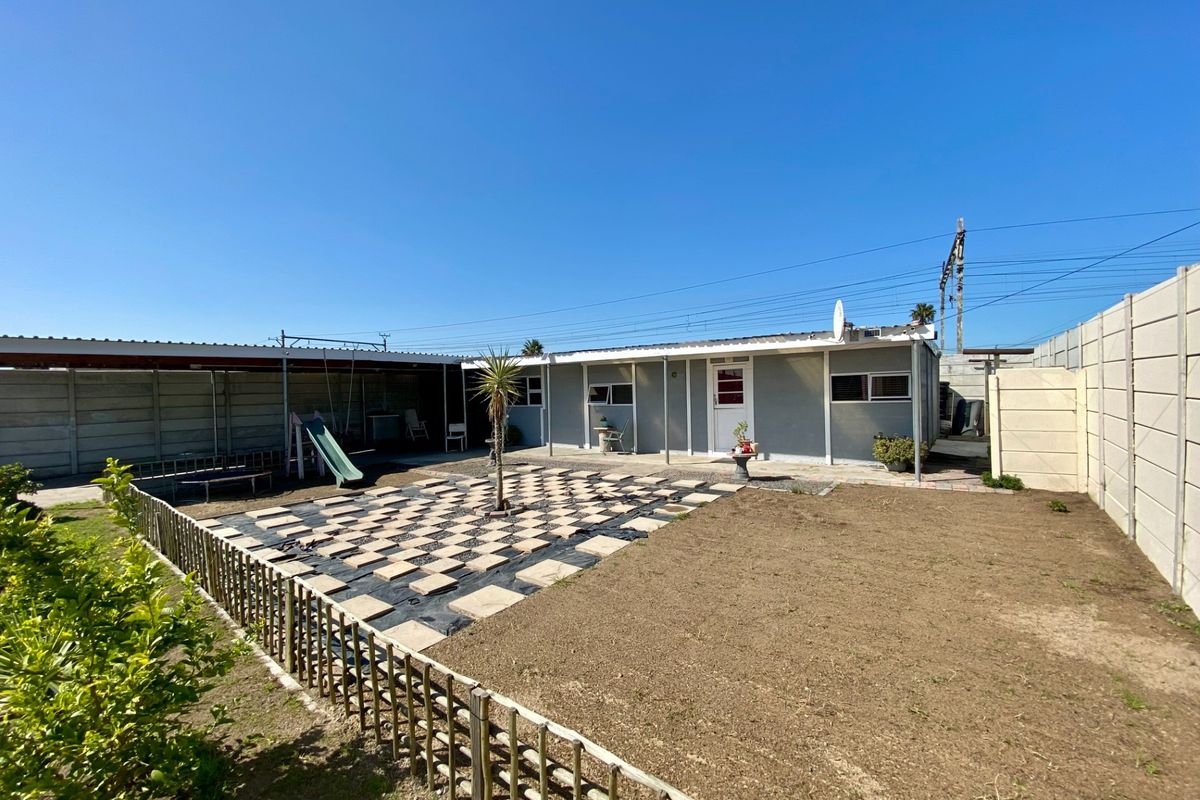 Rear exterior view of the property featuring a paved patio area, corrugated roof structure, and a fenced garden space.