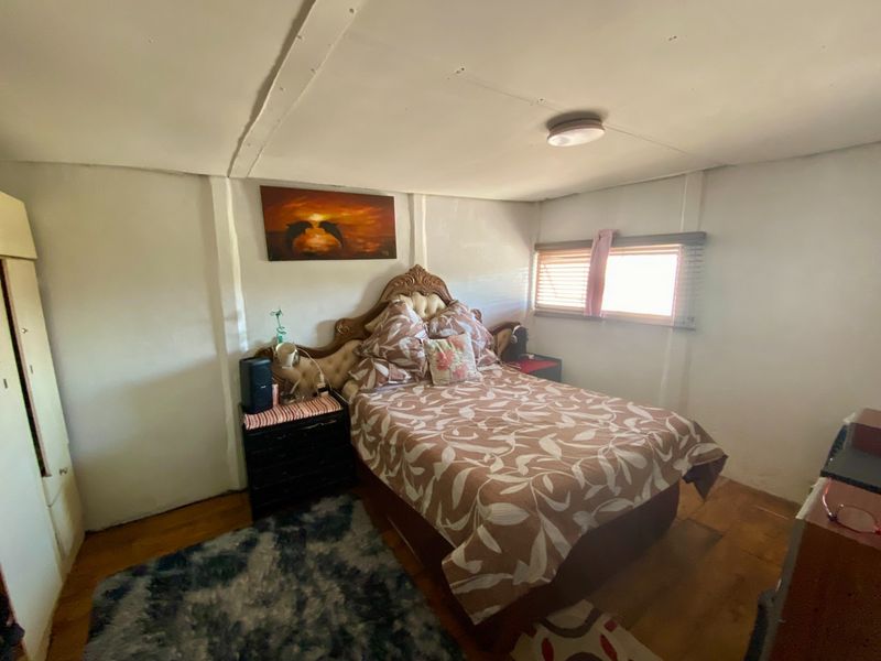 A bedroom featuring timber flooring and a simple ceiling light, showing signs of wear on the ceiling and wall finishes.