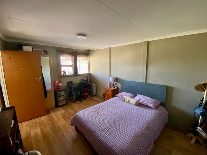 A functional bedroom featuring laminate flooring, neutral wall tones, and natural light through window blinds.