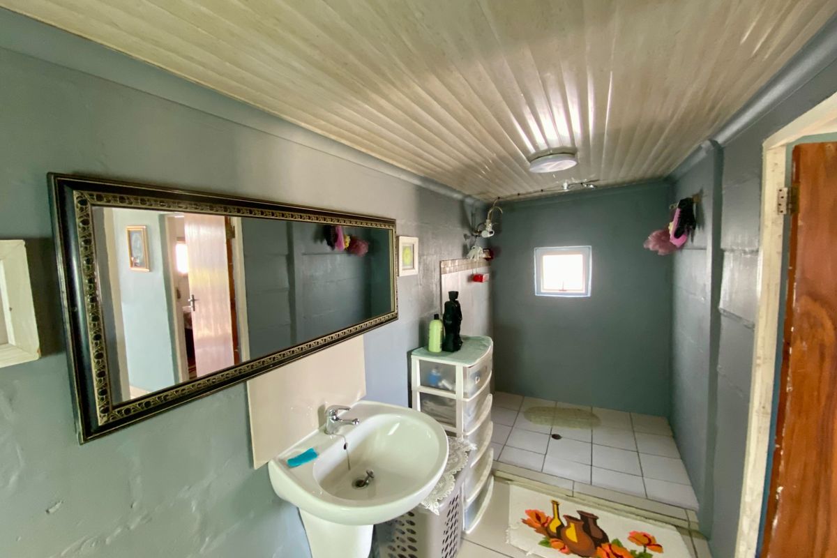 A functional bathroom featuring a wall-mounted basin, tiled flooring with a dedicated shower area, and a timber panel ceiling.