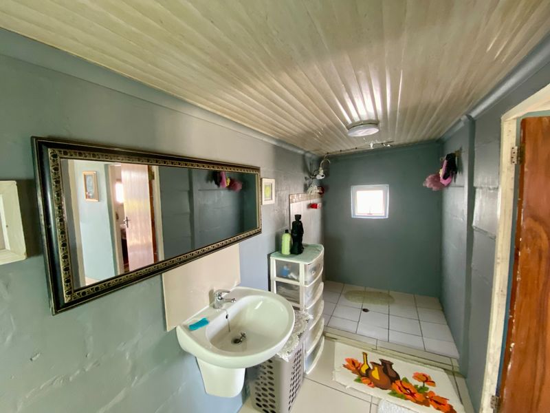 A functional bathroom featuring a wall-mounted basin, tiled flooring with a dedicated shower area, and a timber panel ceiling.