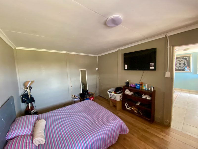 A bedroom featuring laminate flooring and a wall-mounted television, with visible electrical conduit and basic wall finishes.