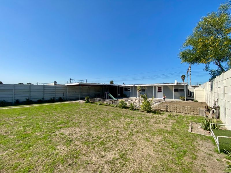 Spacious rear garden featuring a lawn, paved area, and a covered patio, enclosed by a high precast concrete boundary wall.