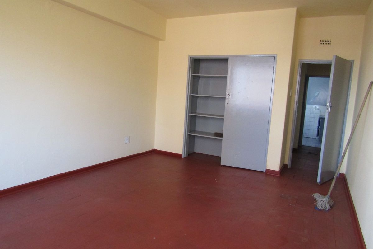 An empty bedroom featuring painted wooden flooring and a built-in cupboard, offering a blank canvas for renovation or interior design updates.