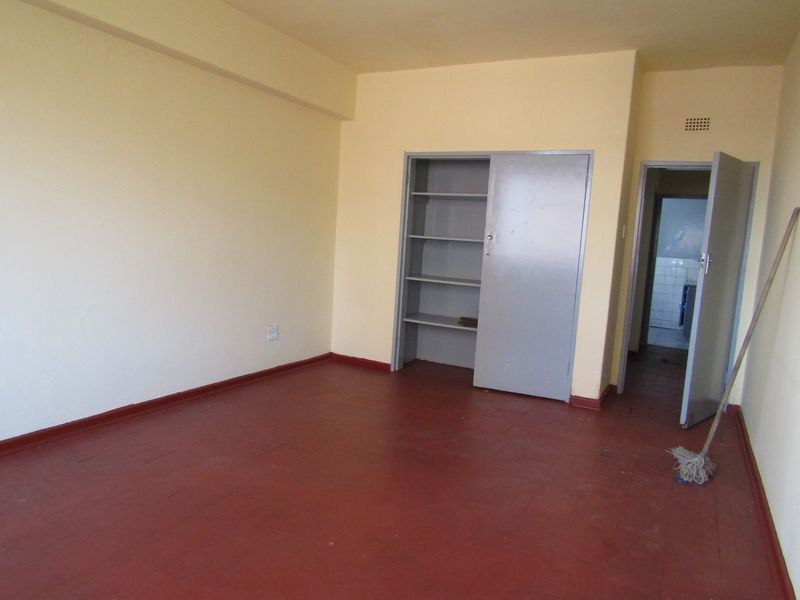 An empty bedroom featuring painted wooden flooring and a built-in cupboard, offering a blank canvas for renovation or interior design updates.