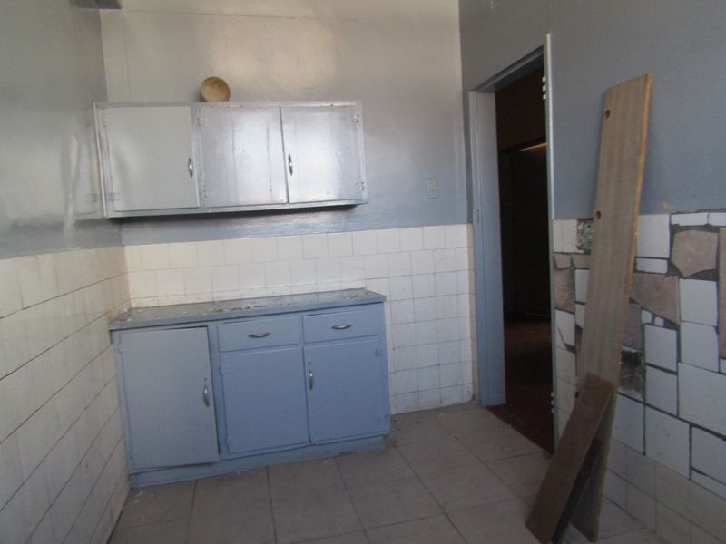A dated kitchen area featuring built-in cabinetry and tiled splashbacks, requiring renovation to modernize the space.