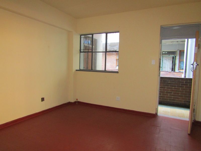 An empty bedroom featuring painted concrete flooring, a steel-framed window, and direct access to an external balcony area.