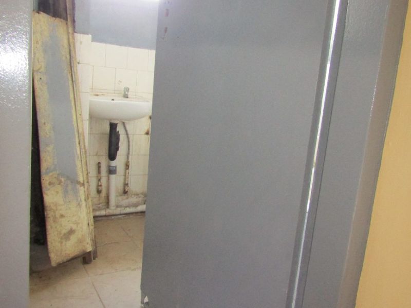 A small, dated bathroom featuring a pedestal basin and tiled flooring, currently in need of significant maintenance and cosmetic updates.