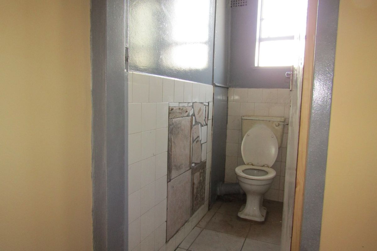 A small, dated bathroom featuring a toilet, tiled flooring, and partially tiled walls in need of repair and modernization.